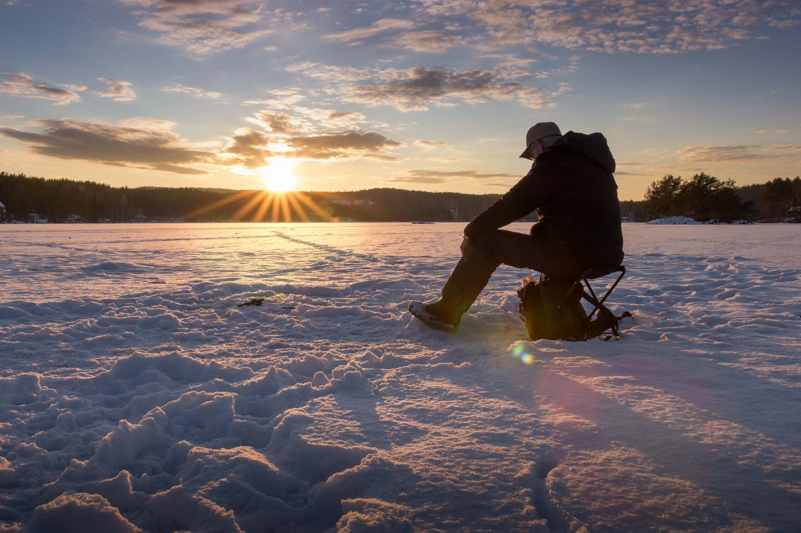 Ice fishing on a lake in Norway at sunset.